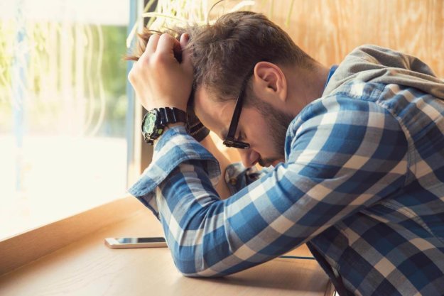 Young depressed man sitting at table with mobile phone in cafe